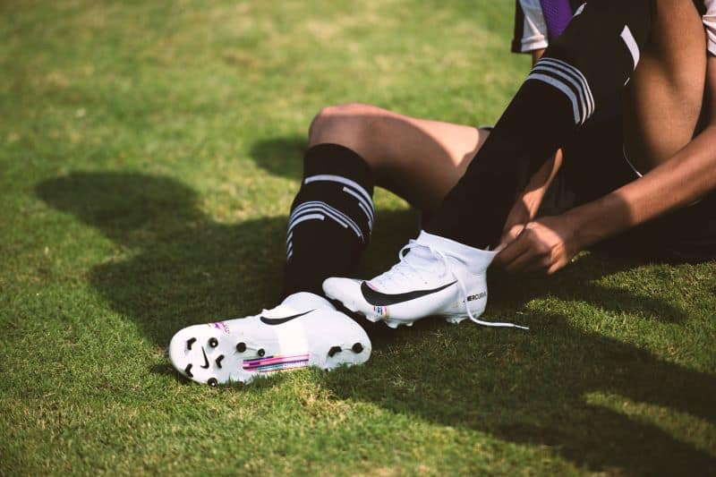 soccer player putting on white and black cleats on the field