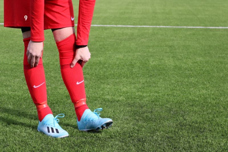 red-jerseyed soccer player with sea-blue colored lightweight cleats